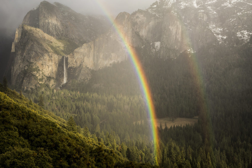 Rainbow arcing across Yosemite Valley beneath sunlit granite cliffs