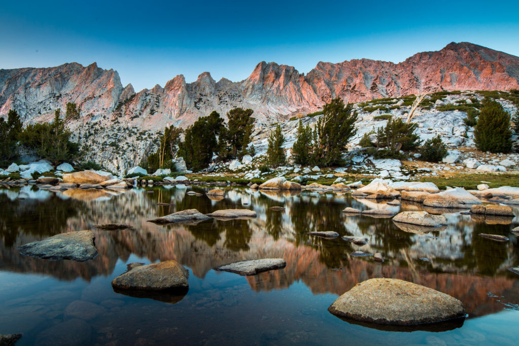 Granite boulders reflected in a still alpine lake beneath mountain peaks