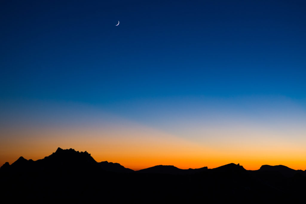 Crescent moon above silhouetted mountain peaks at sunset