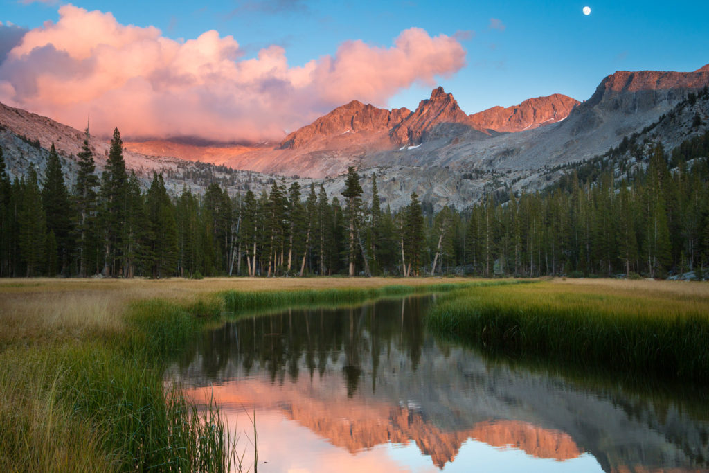 Pink alpenglow on mountain peaks reflected in a quiet forest lake