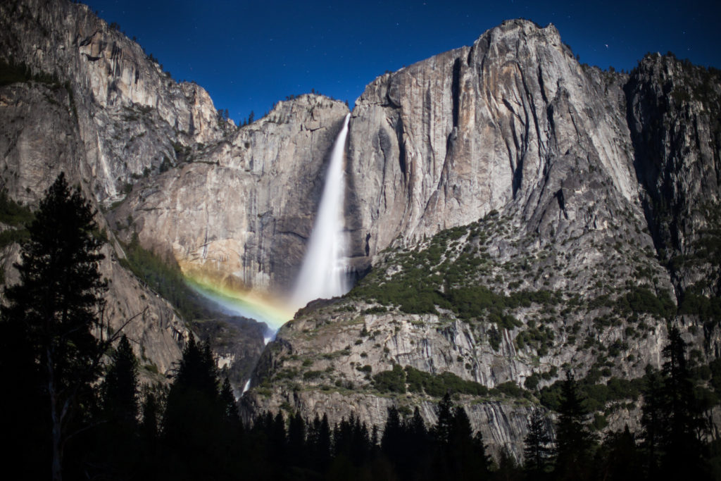 Rainbow at the base of Yosemite Falls beneath a clear blue sky
