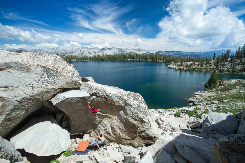 Climber beneath a granite overhang beside a blue alpine lake