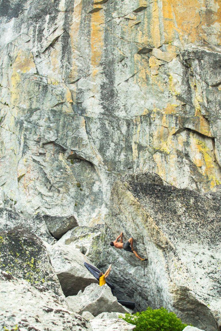 Climber on a tall fractured rock face above a boulder field
