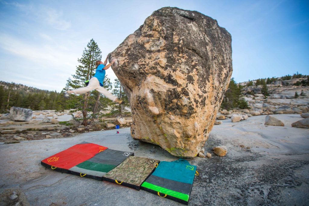 Boulderer reaching up a rounded granite rock above colorful crash pads