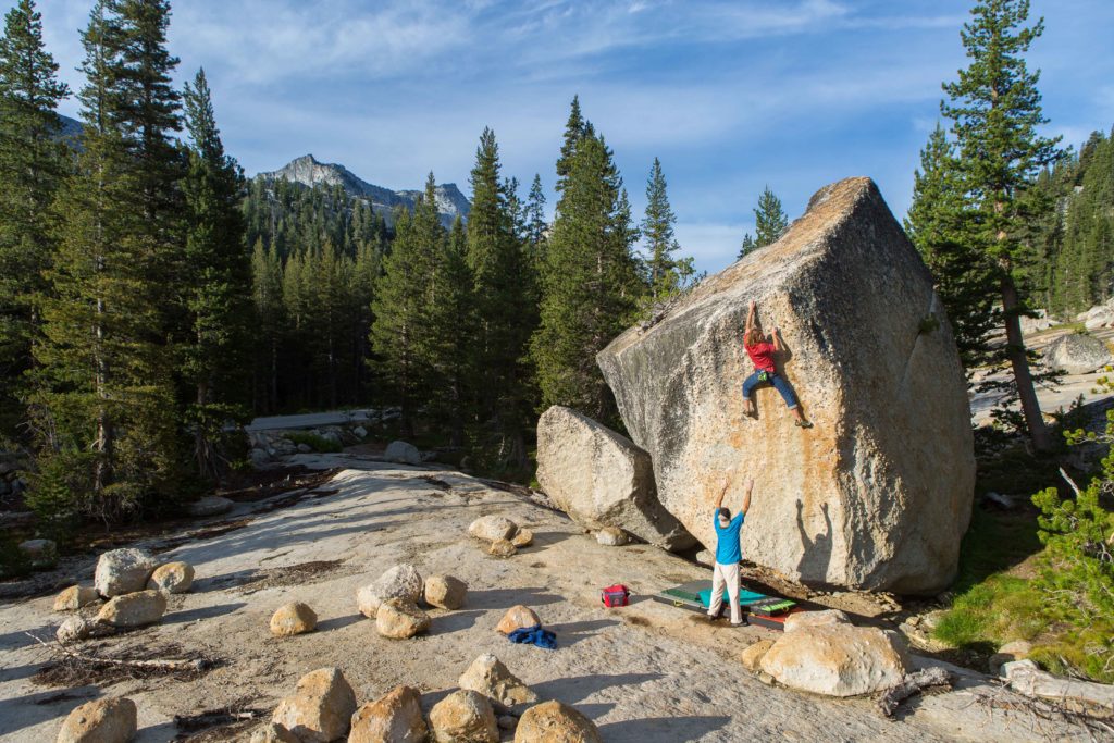 Climber ascending a freestanding forest boulder with a spotter below