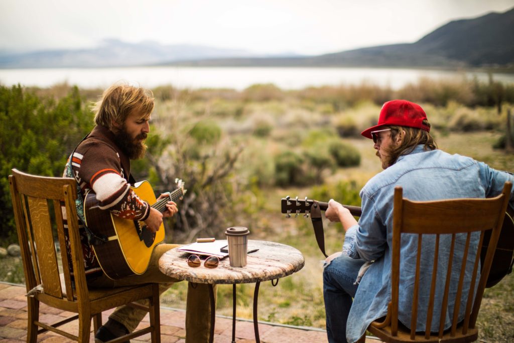 Two people playing guitars outdoors beside an open meadow