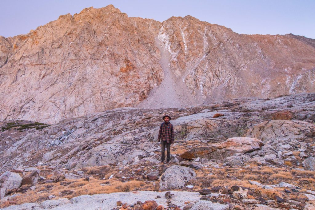 Hiker on a rocky slope beneath a sunlit granite mountain