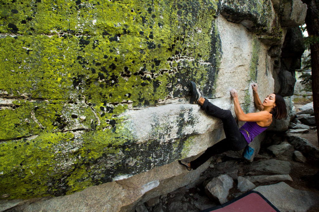 Climber in a purple top reaching across a lichen-covered rock face