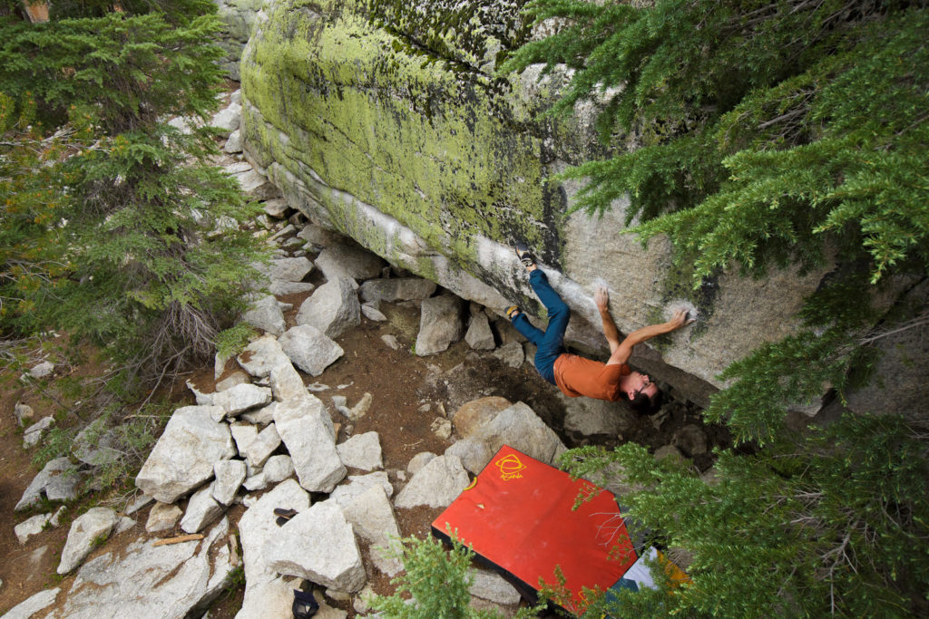 Boulderer beneath a forest rock overhang above a red crash pad