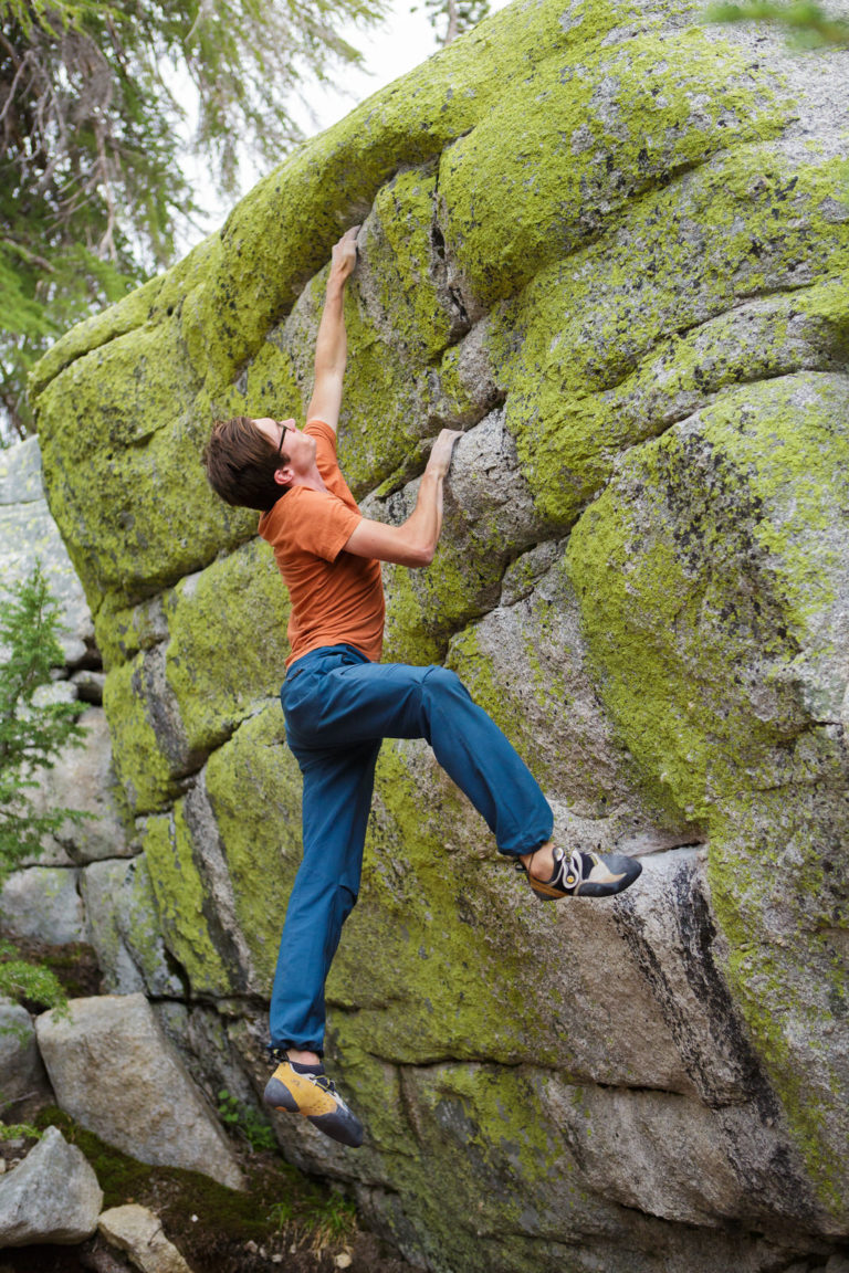 Climber gripping a lichen-covered boulder in the forest