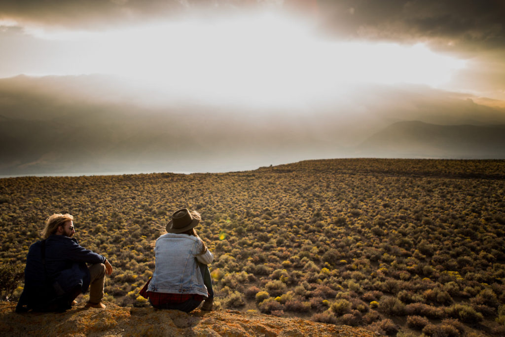 Two people sitting above a broad valley in low evening light