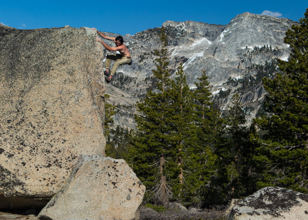 Climber high on a granite boulder with a mountain wall behind