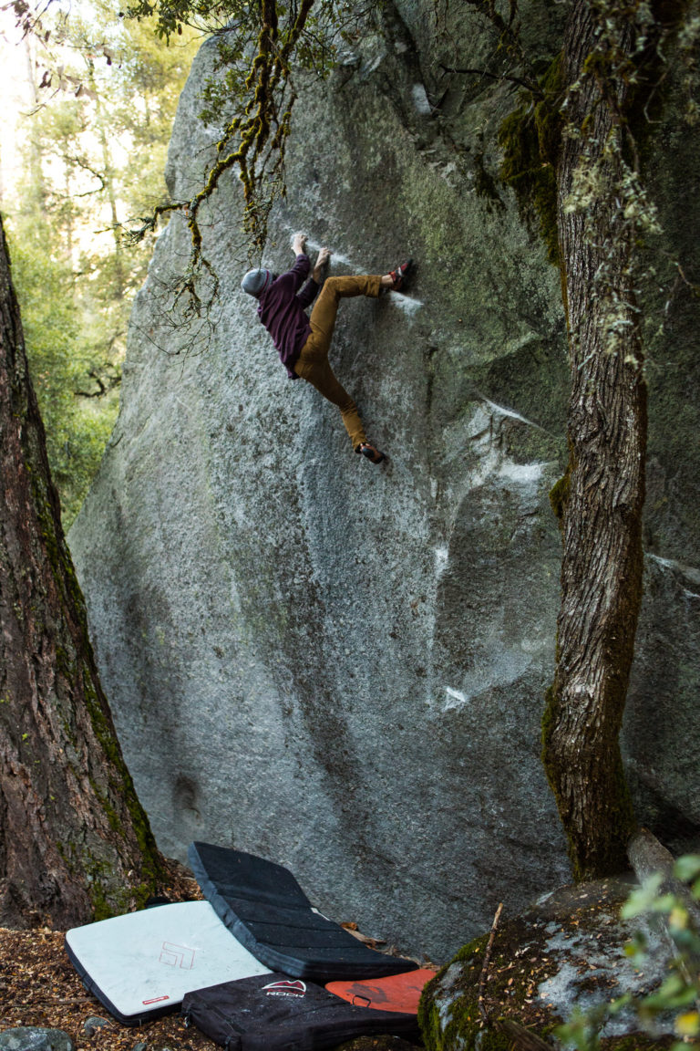 Climber on a tall shaded boulder above crash pads