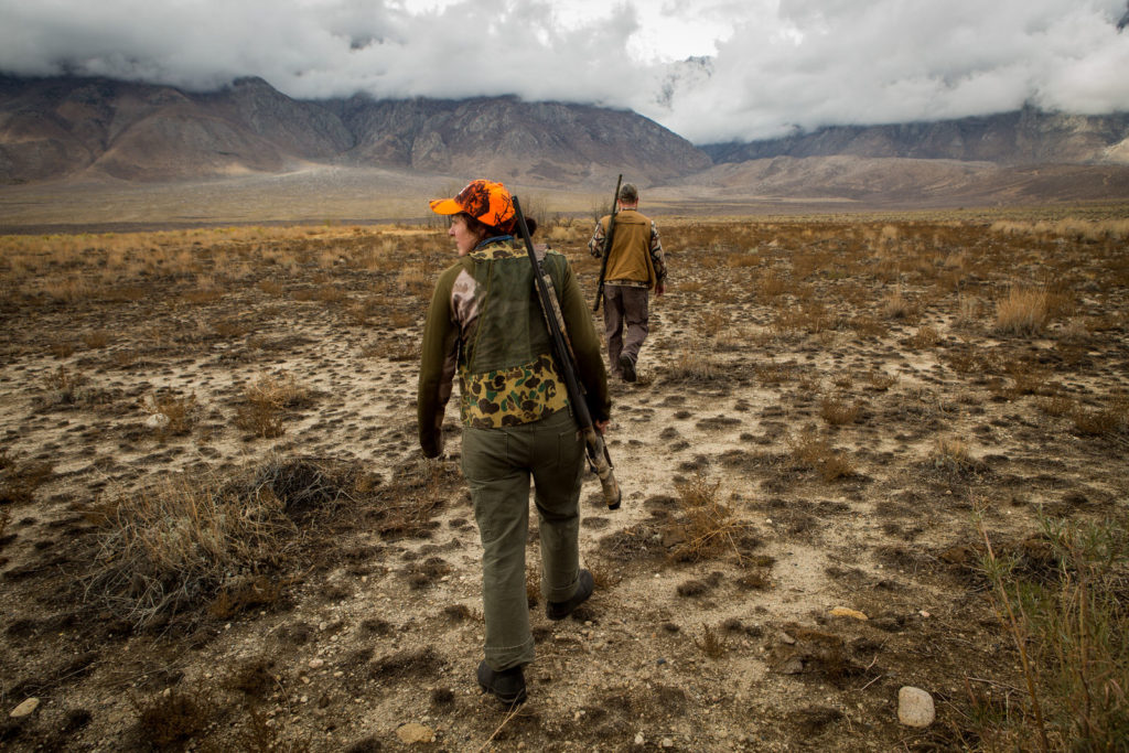 Two hunters walking across open sagebrush toward distant mountains