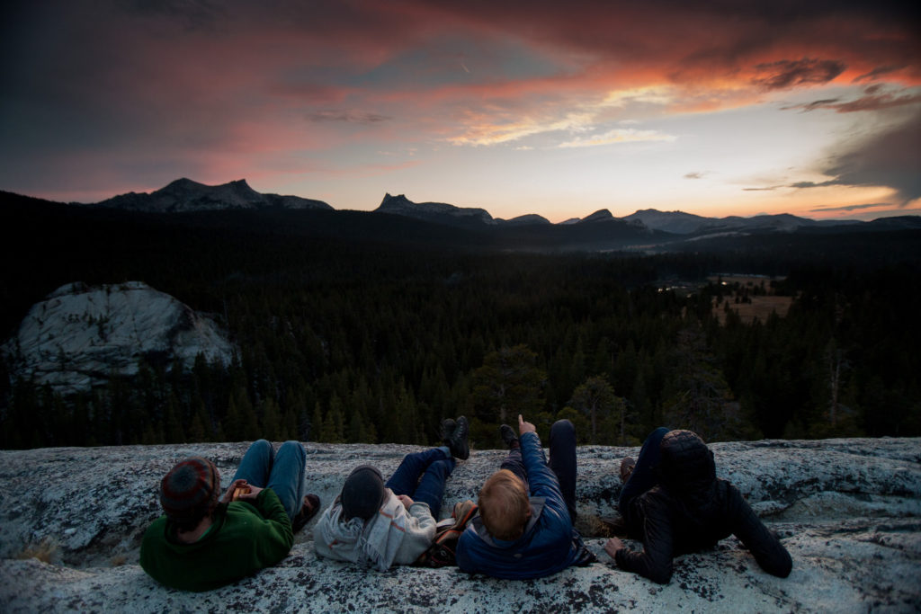 Friends resting on a granite overlook beneath a colorful sunset