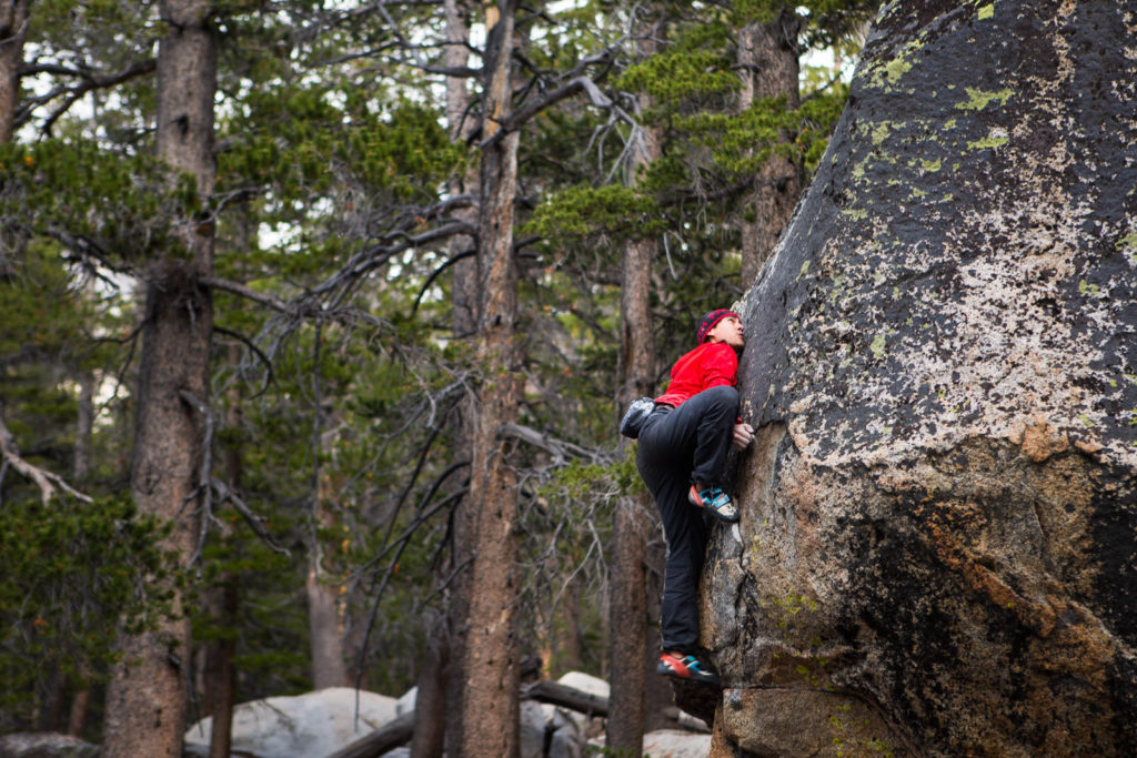 Climber in a red top ascending a forest boulder