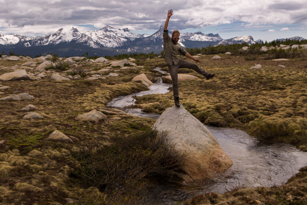 Hiker balancing on a granite boulder in an alpine meadow