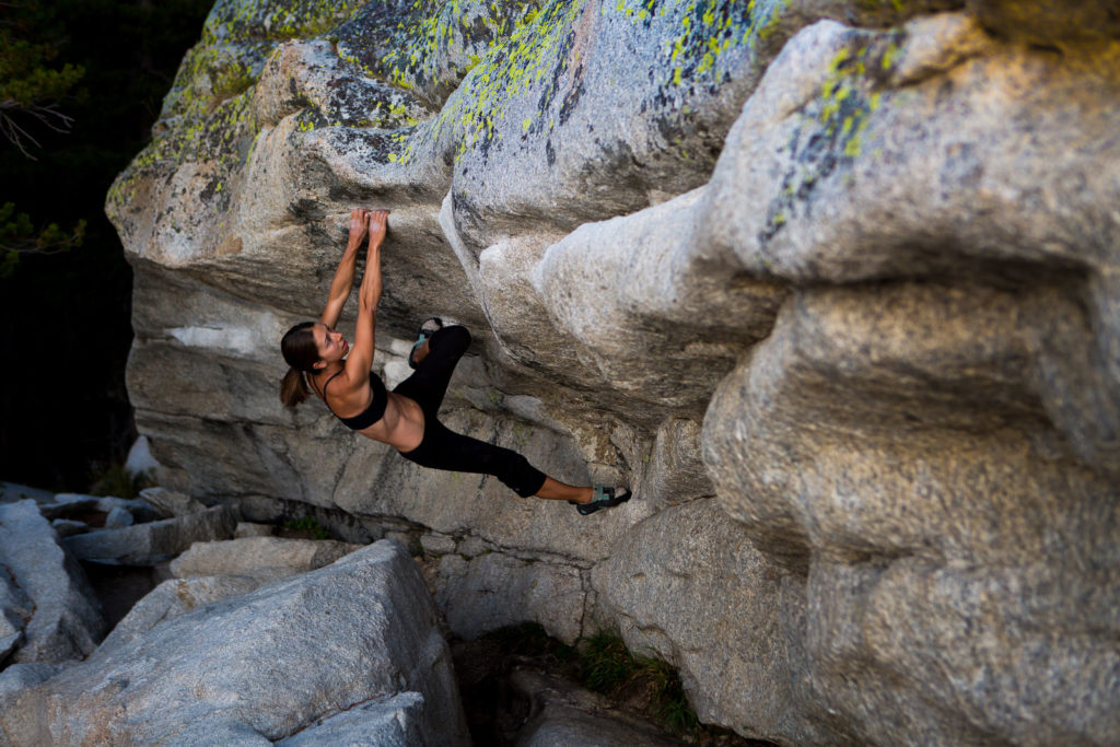 Boulderer hanging beneath a granite overhang above crash pads