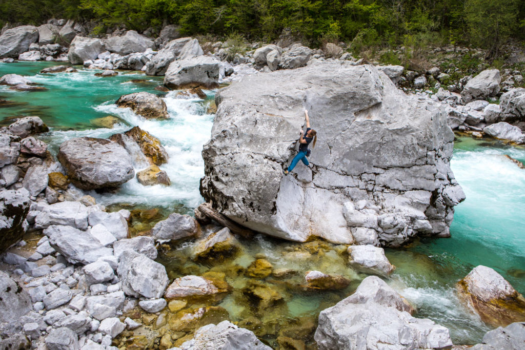 Climber traversing a large boulder beside turquoise river rapids
