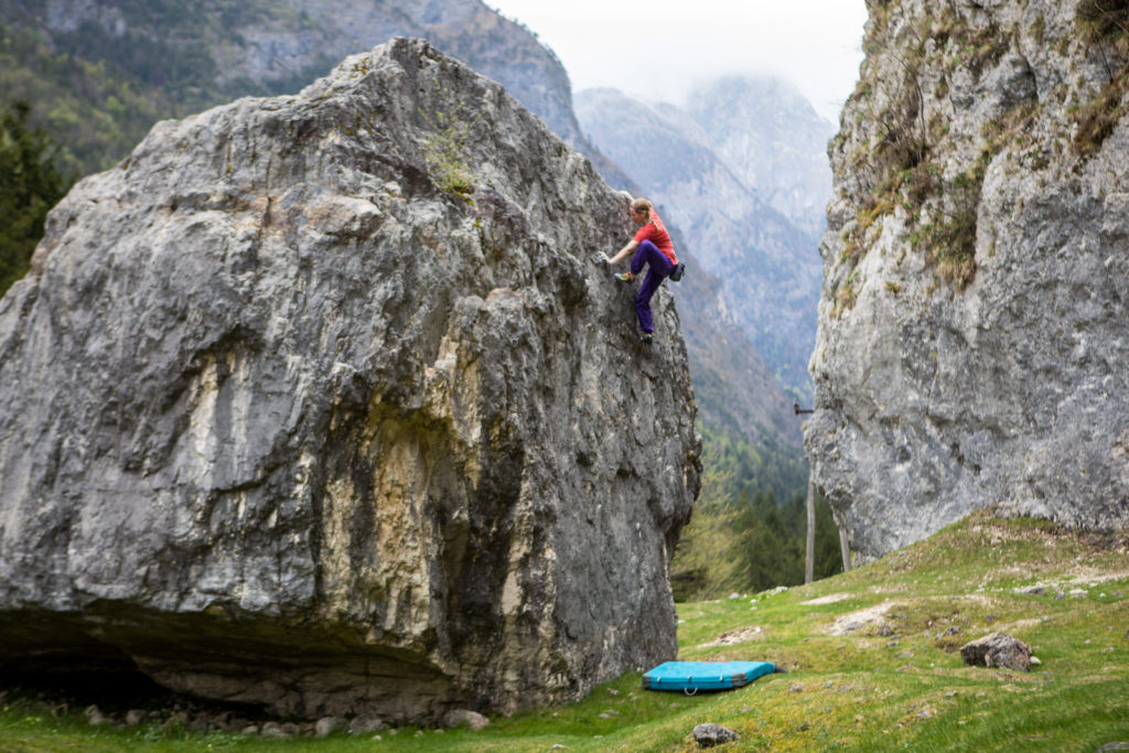 Climber ascending a tall freestanding boulder above a crash pad