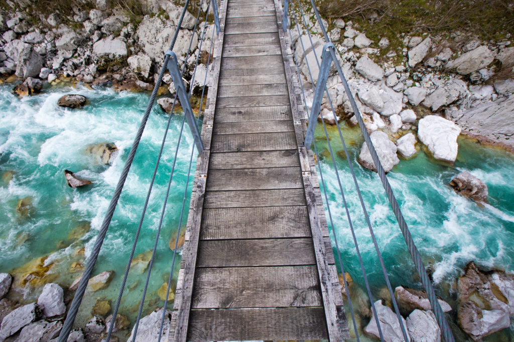 Narrow suspension footbridge over a turquoise mountain river