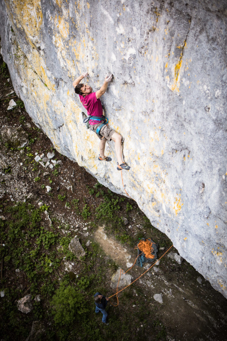 Rock climber in a pink top scaling a steep limestone wall