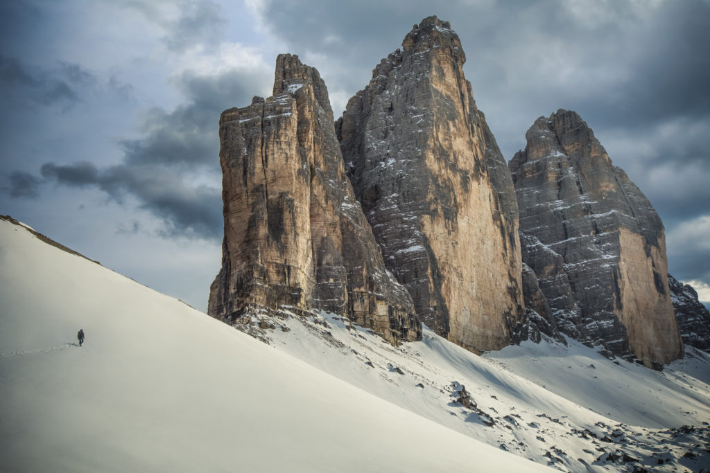 Lone hiker crossing a snowfield beneath towering rock spires