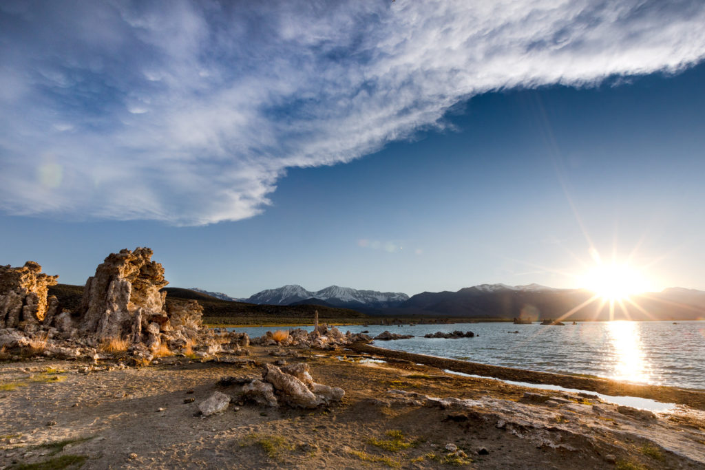 Sunrise beside lakeshore rock towers and distant mountains
