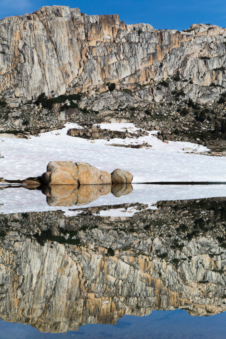 Snow-covered granite basin reflected in still water