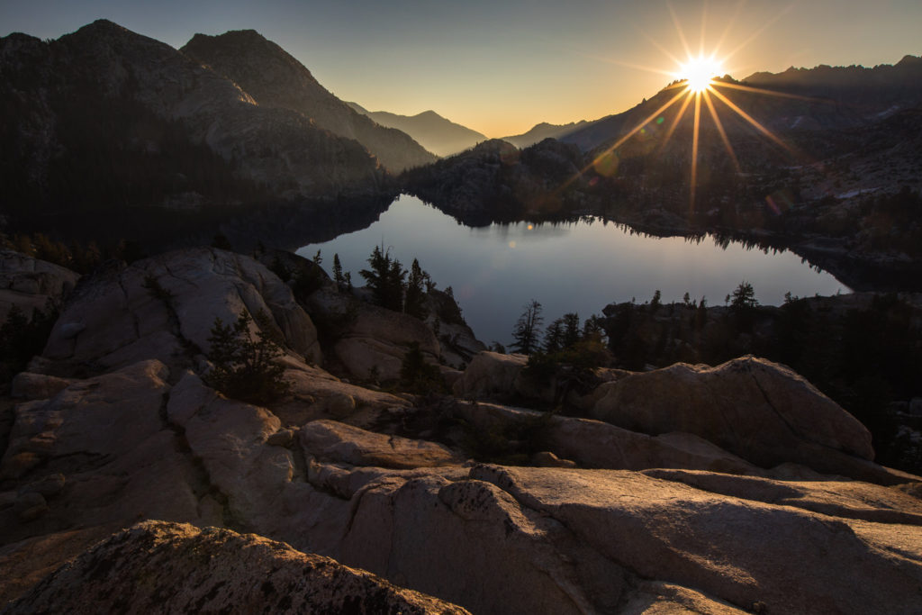 Sunburst above a still alpine lake framed by rocky mountain slopes