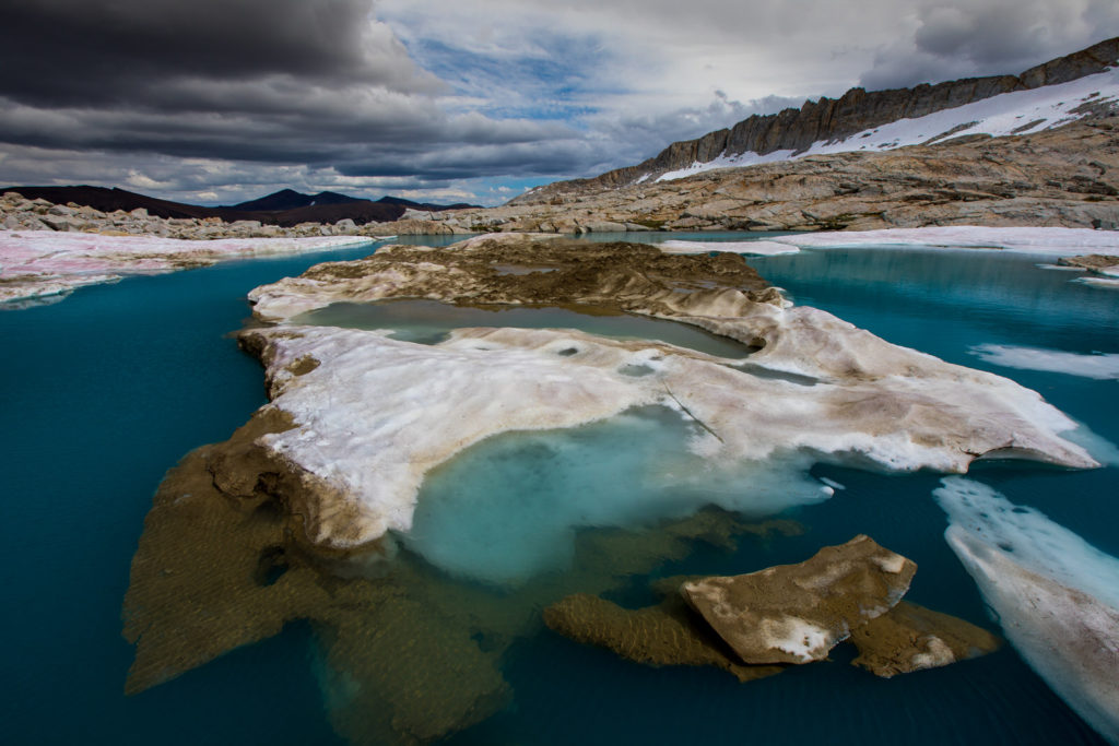 Turquoise alpine water surrounded by melting snow and granite