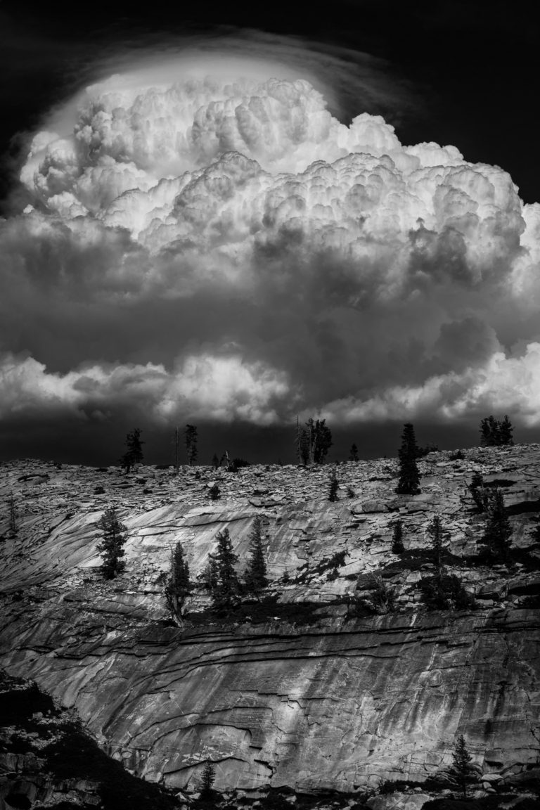 Black-and-white thundercloud towering above granite slopes and pines