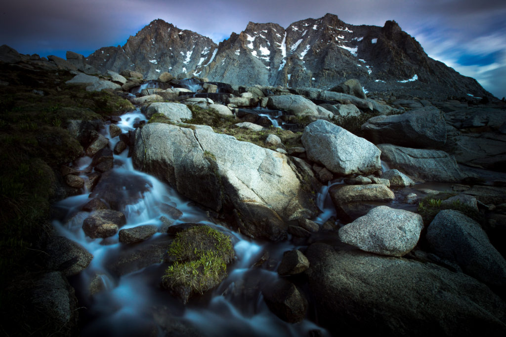 Alpine stream cascading between granite boulders below rugged peaks