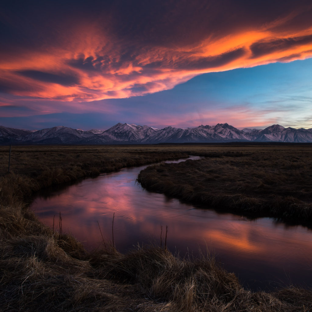 Orange sunset clouds reflected in a winding meadow stream
