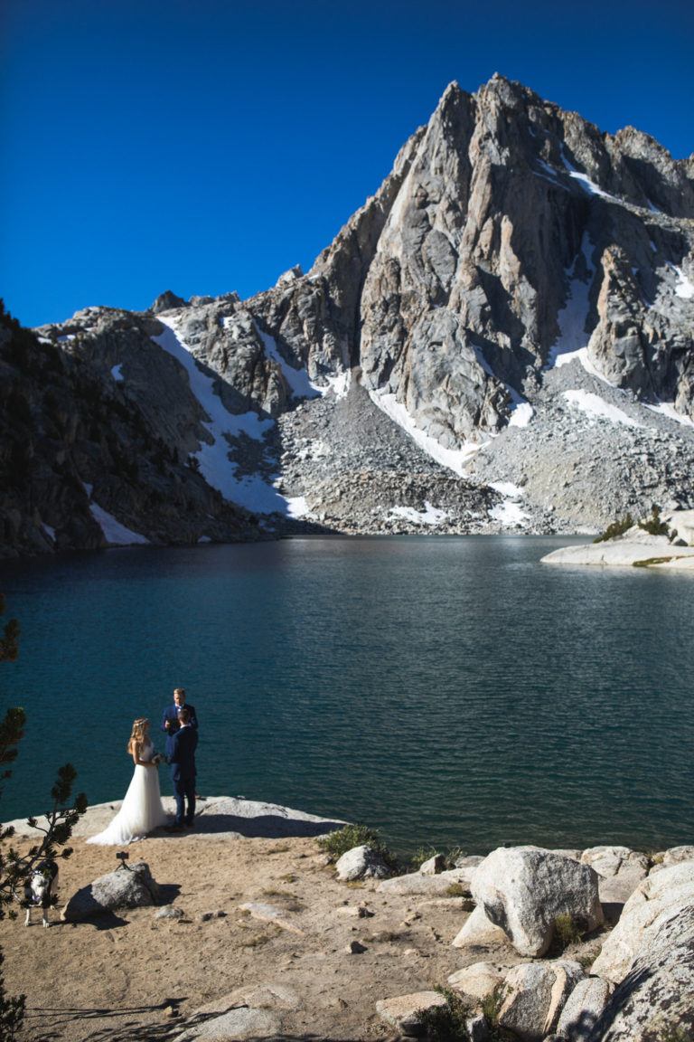 Tiny wedding party beside an alpine lake below a towering granite peak