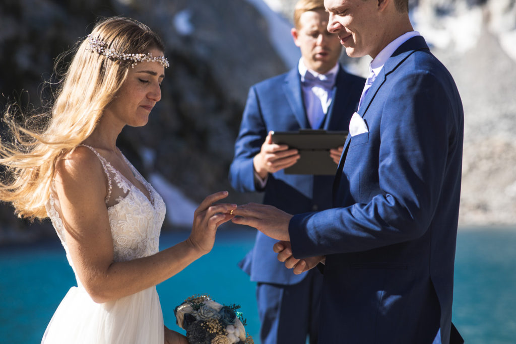 Bride and groom exchanging wedding rings with their officiant behind them
