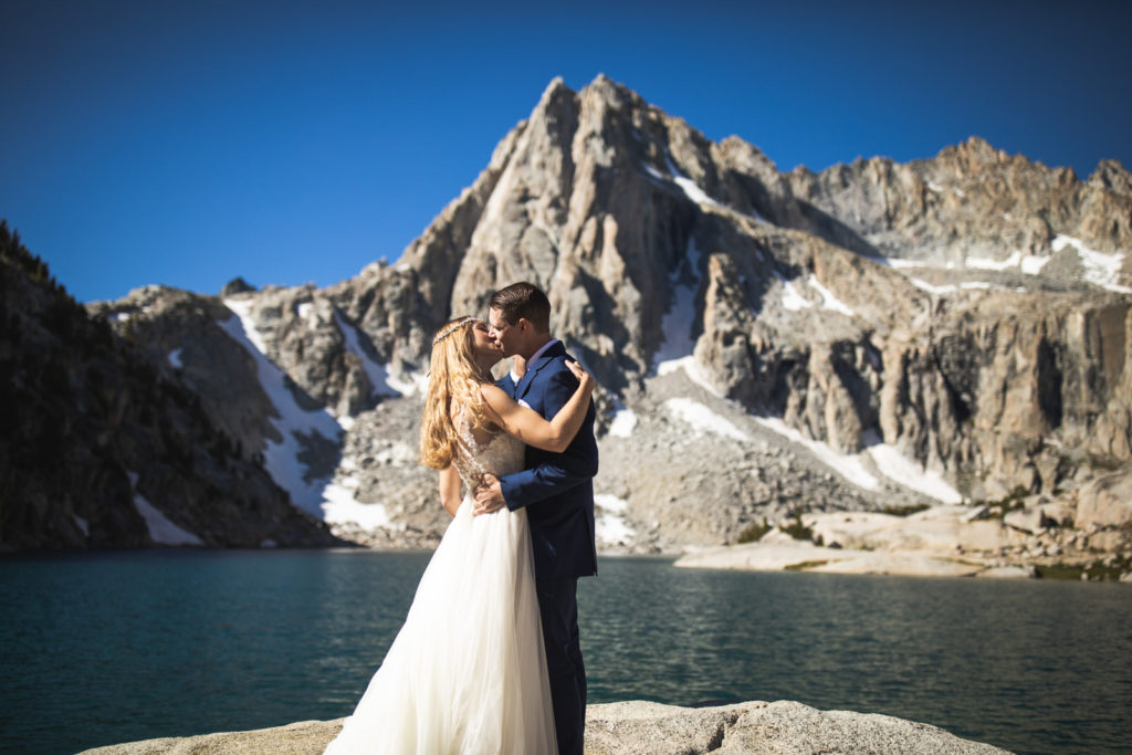 Newlyweds kissing in front of an alpine lake and jagged peaks