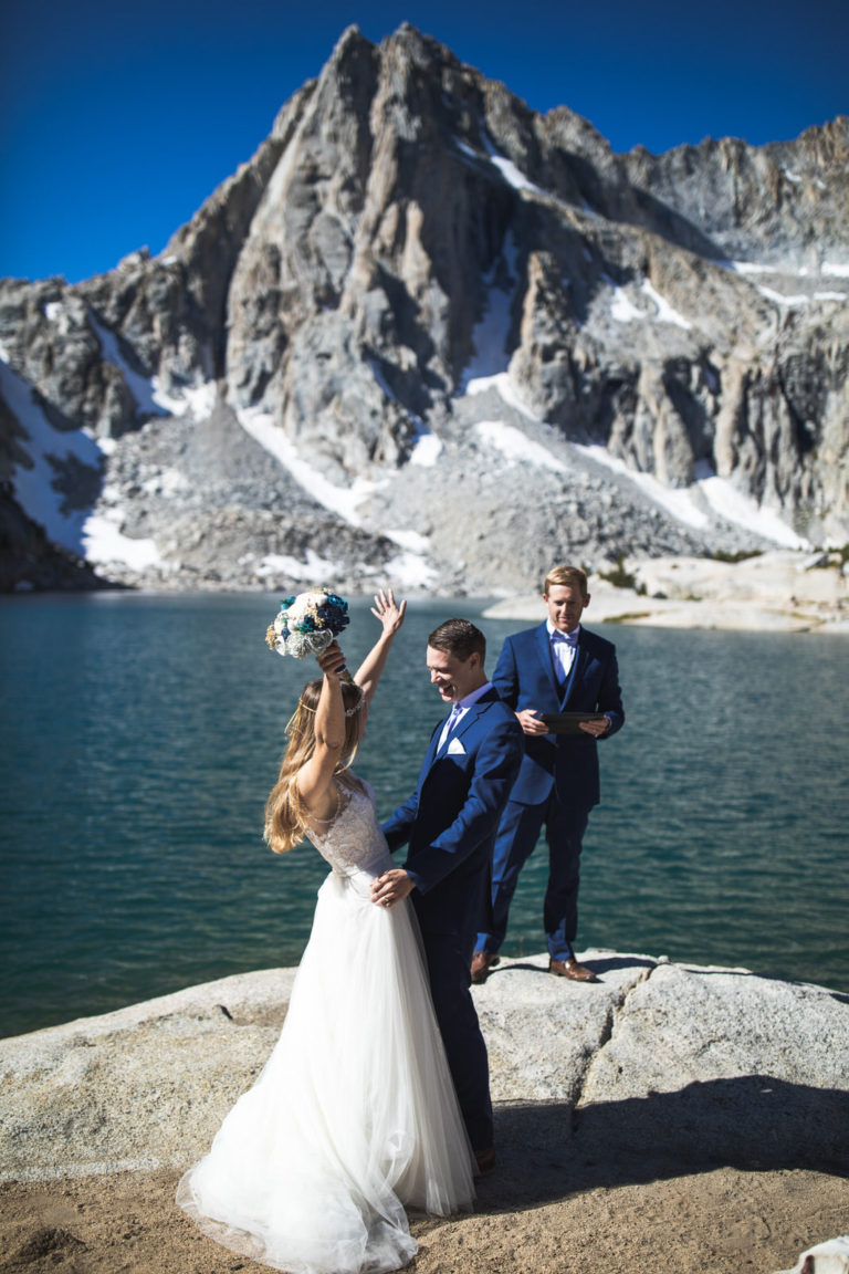Bride raising her bouquet after the lakeside ceremony