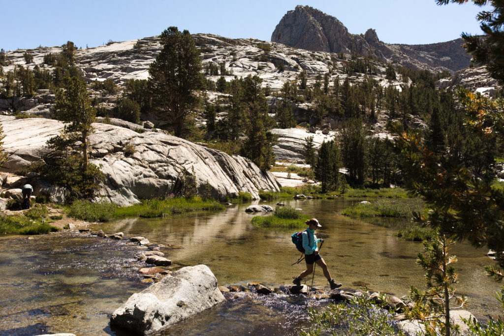 Backpacker crossing a shallow stream in a granite basin