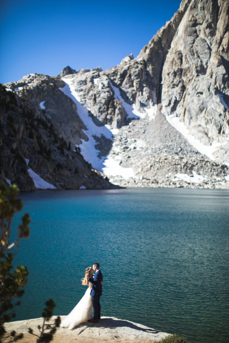 Wedding couple on the shore of a blue alpine lake beneath granite cliffs