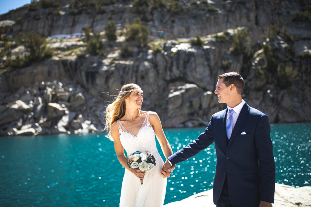 Bride holding a bouquet and the groom’s hand beside turquoise water