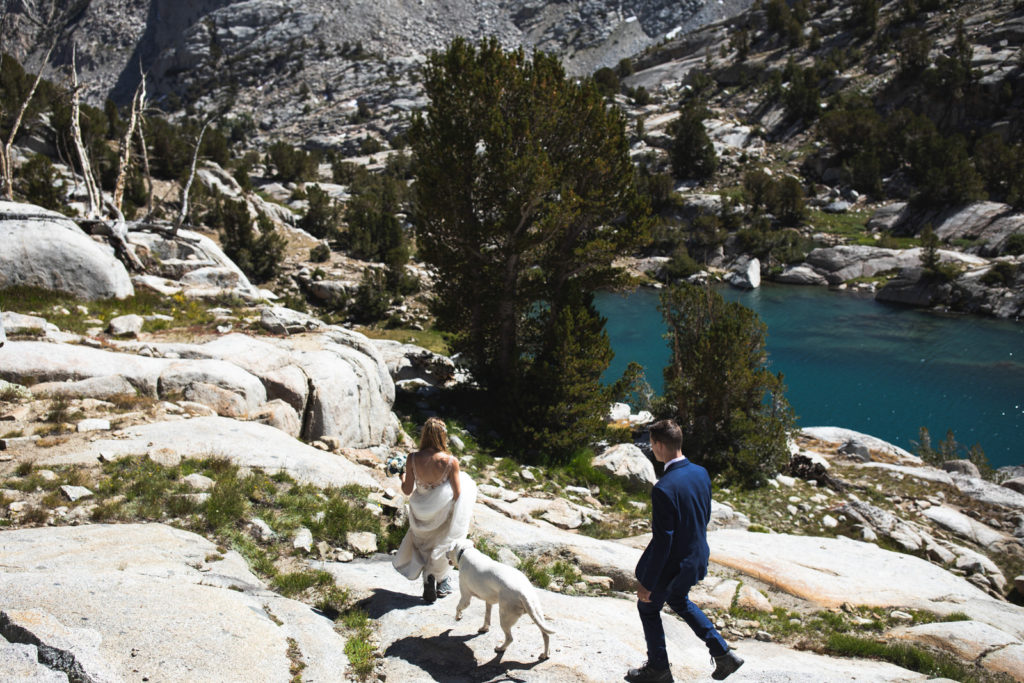 Wedding couple walking across granite above a blue mountain lake