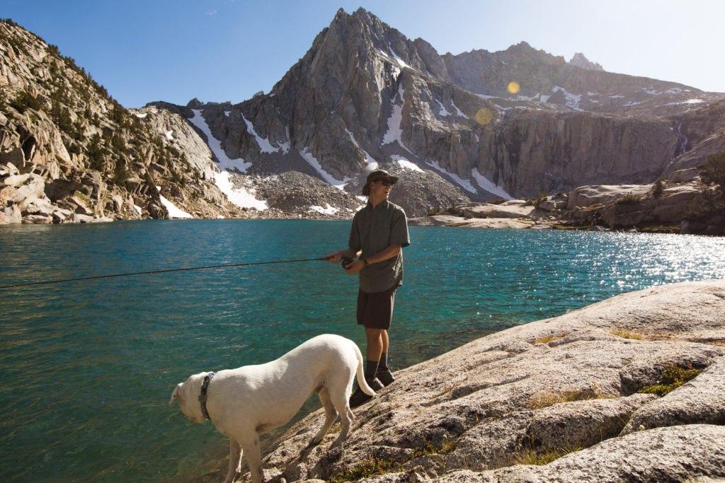 Hiker and white dog beside a turquoise mountain lake