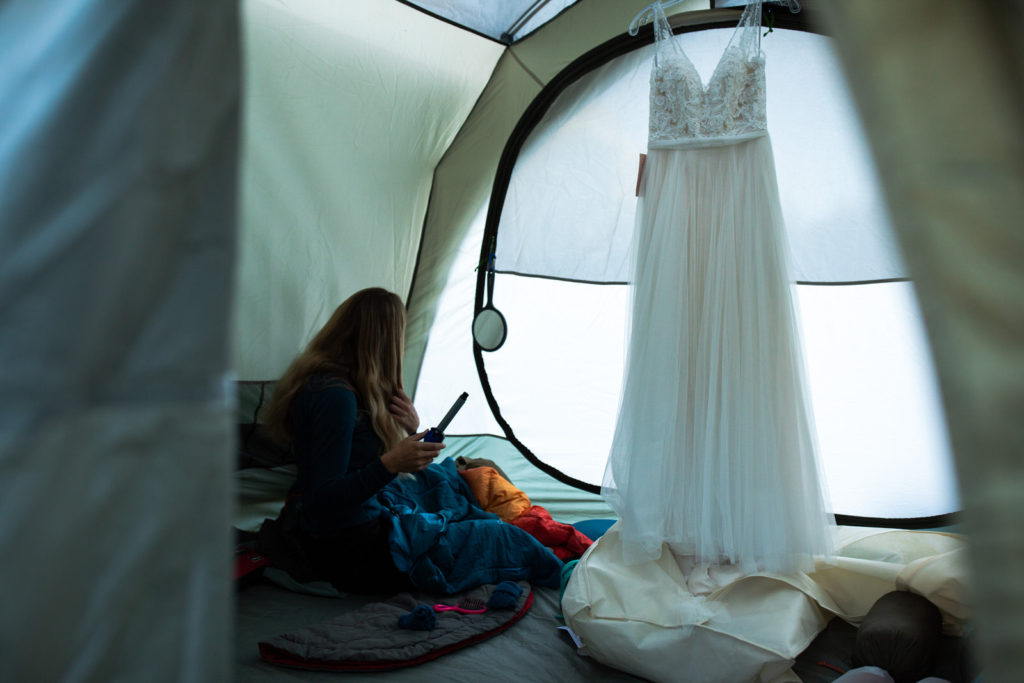 Bride getting ready inside a tent with her wedding dress hanging nearby