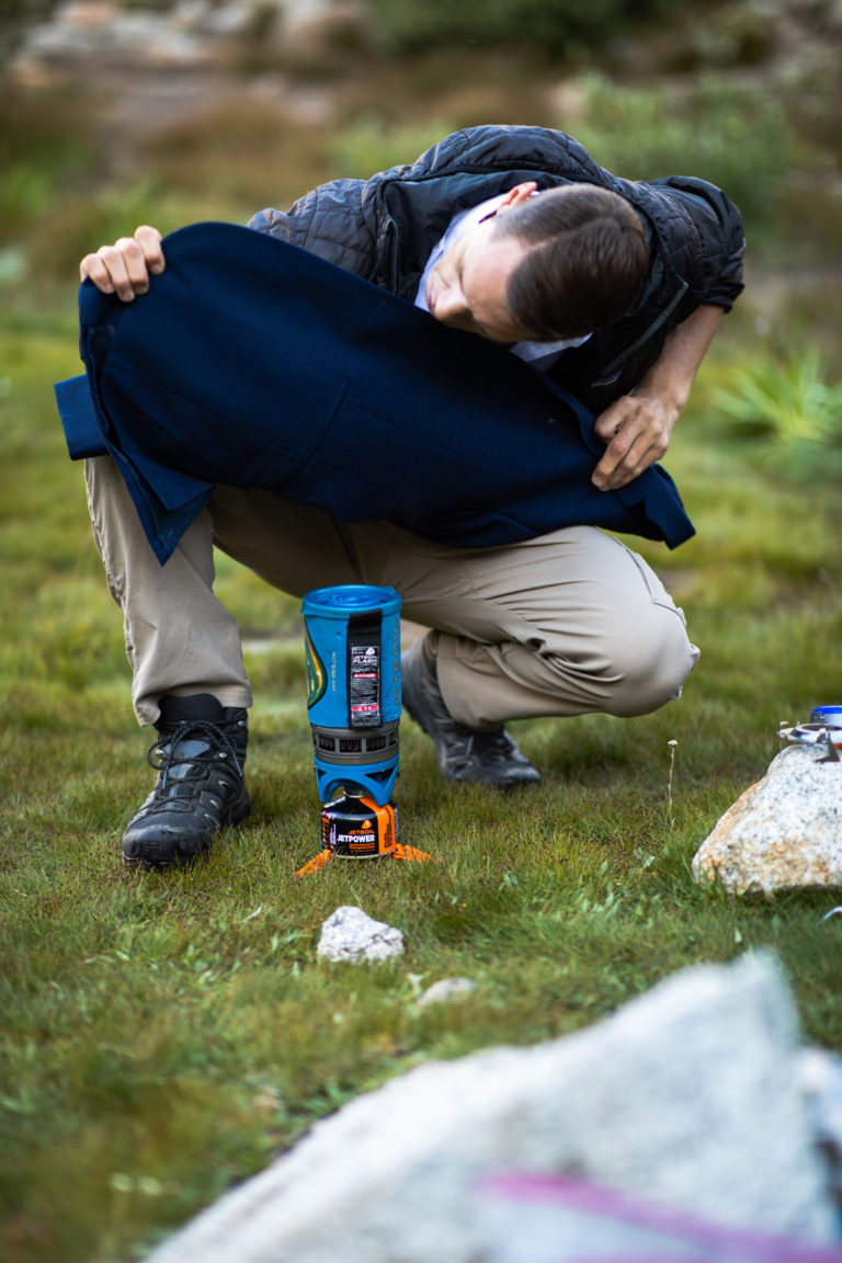 Man holding a suit jacket above a small camping stove