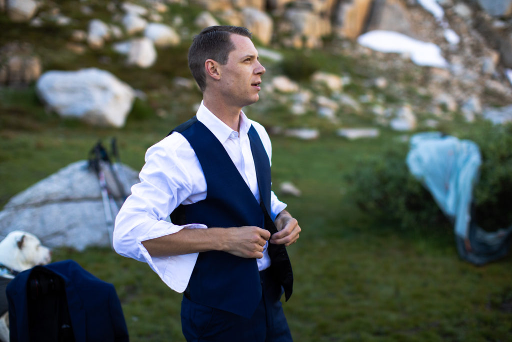 Groom buttoning his vest at a mountain campsite