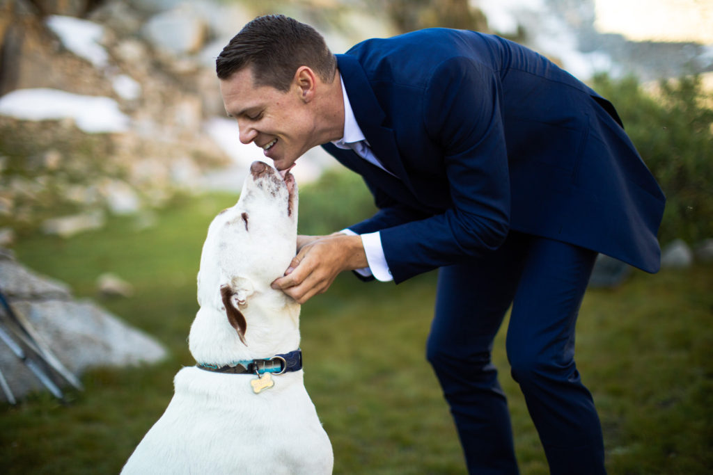 Groom greeting a white dog at the campsite