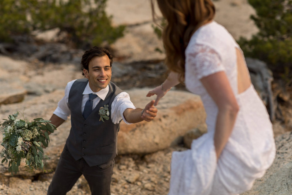 Groom reaching for the bride’s hand on a rocky trail