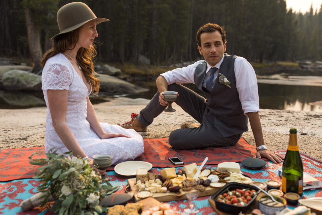 Newlyweds enjoying a picnic beside a forest lake