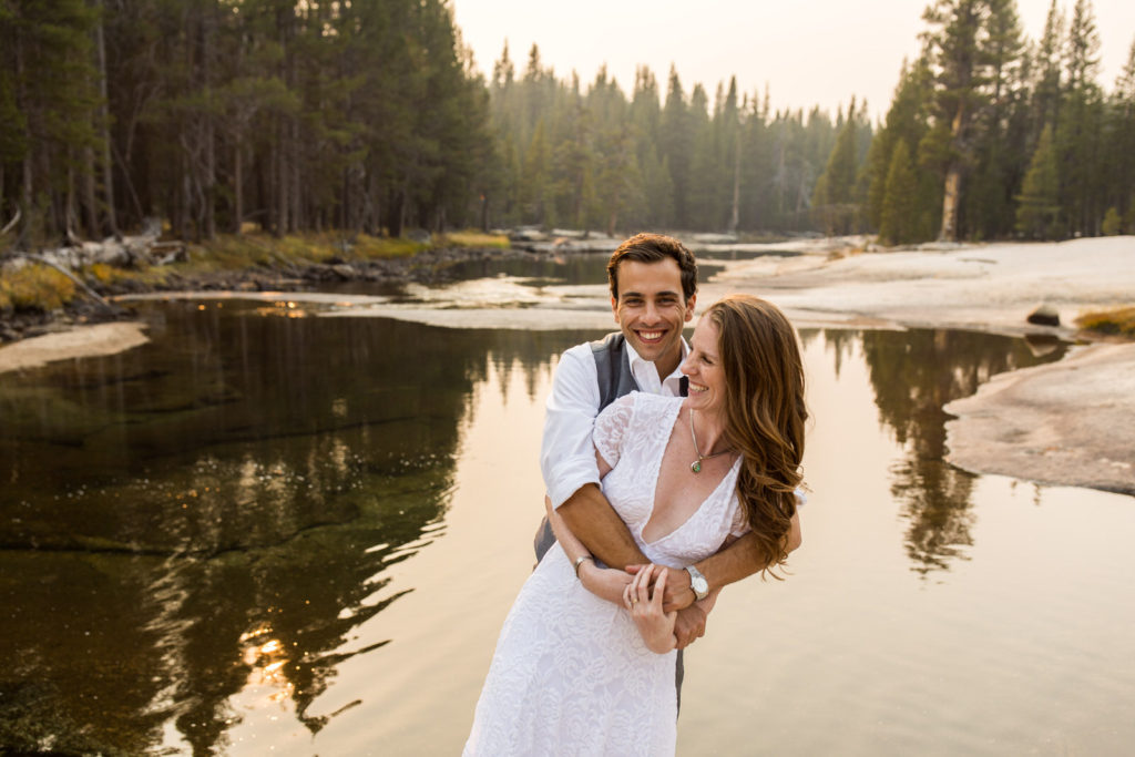 Groom lifting the bride beside calm reflective water